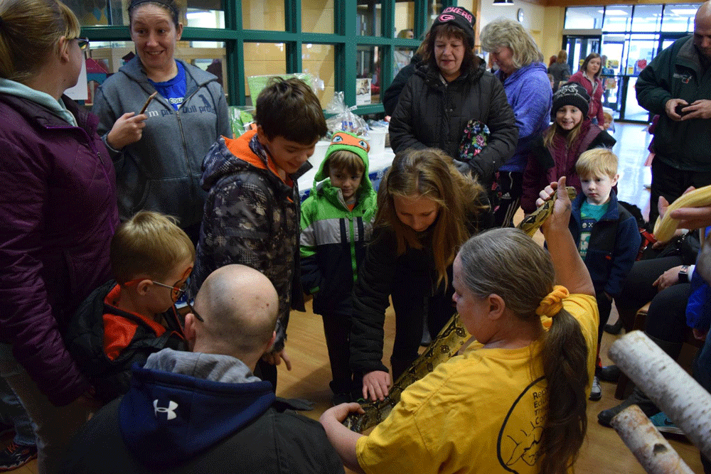 Woman holding a snake in front of a small crowd.